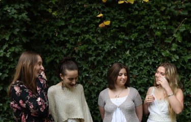 Four singers in a line against a green tree