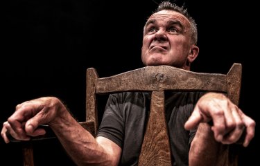 A man pulling a silly afce looking with chin resting on a chair