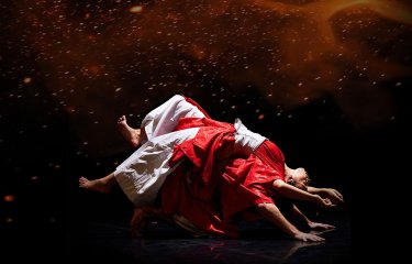 Two dancers performing in white and red outfits with a dark and moody black and red background