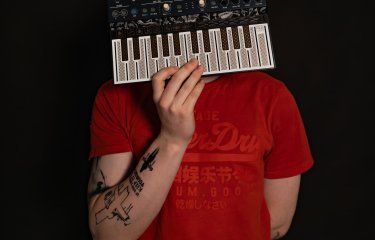 A person wearing a red t-short holding a small midi keyboard in front of their face