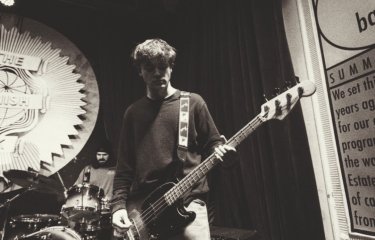 A black and white photo a someone performing on stage playing the bass guitar