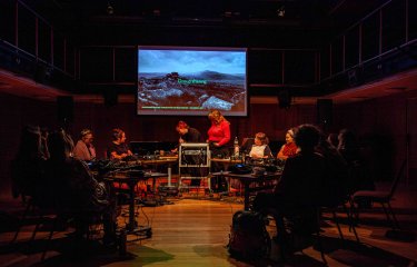 Gr group of musicians at various stations in a circle interacting and performing electronic music