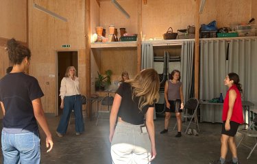 A group of performers in a theatre workshop anwooden room with a green floor
