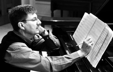 A black and white photo of a composer sat at a piano