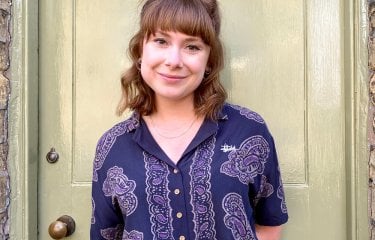 A woman in front of a door wearing a purple shirt