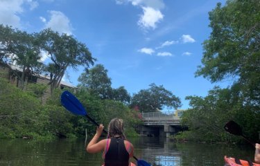 A girl in an orange kayak on the water with trees