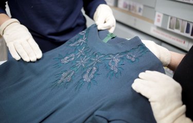 Close crop of two people wearing white gloves examining a garment in the Textiles & Dress Collection