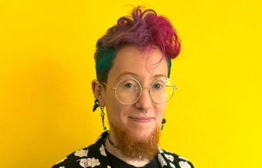 A person smiling into the camera against a yellow background