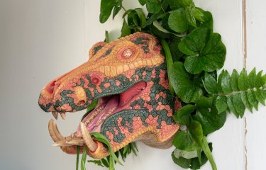A multi-coloured velociraptor head is adorned with leafy green plants