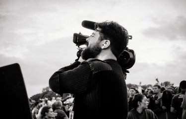 Place and white image of a man using a film camera with a crowd in the background