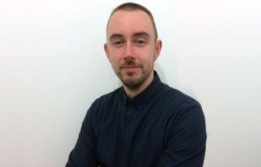 A headshot of Dr John Finnegan sat against a white wall