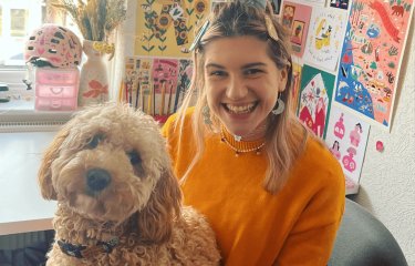 A young woman wearing an orange jumper with a dog on her lap