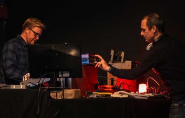 Two men on a stage using analogue equipment to perform a live film score