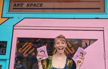 A woman stood outside a pink building holding maps