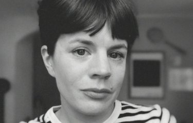 A woman with dark hair wearing a stripy top looking into the camera