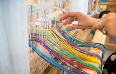 A hand using a weaving machine with multi-coloured wool
