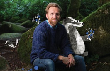Huw Lewis Jones sitting in the woods with an illustration of a badger, bird and flowers