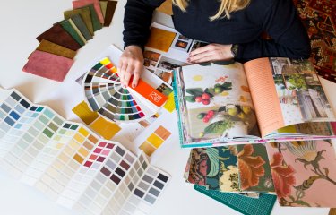 A student on interior design sitting at a table with books, paint and fabric samples in front of them