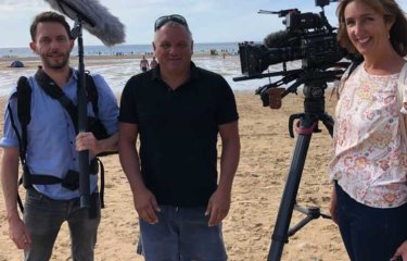 Three people stood on a beach with cameras and filming equipment