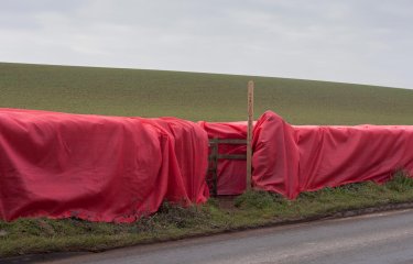 Large red material draped over a wooden fence with a public footpath sign