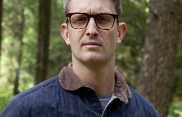 A man wearing glasses stood in a woodland 