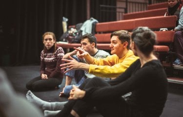 Group of students sat in performance space discussing acting