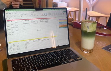 A laptop with excel open and a drink next to it