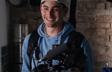 A young man in a backwards cap holding a large camera