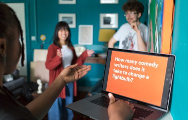 3 people stood round a laptop laughing