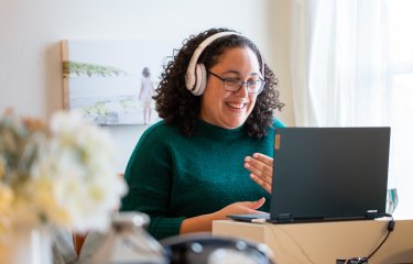 A woman wearing headphones smiling into her computer screen