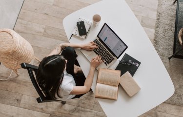 A birds eye view shot of a woman sitting at a desk with laptop and notepad