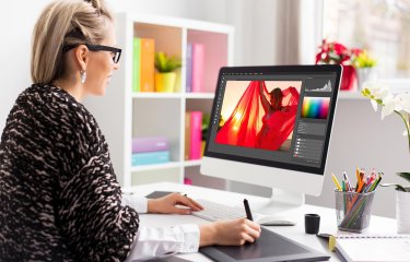 A woman working on an iMac editing a photograph of a woman in a red shawl