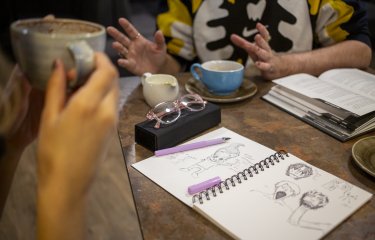 A photo of two students drinking coffee with drawings on the table