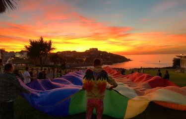 A large rainbow flag is held aloft at sunset