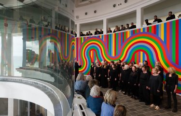 Line of people wearing black infront of rainbow background at Tate St Ives