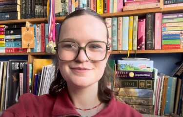 A Falmouth University student smiling at the camera, behind a book case