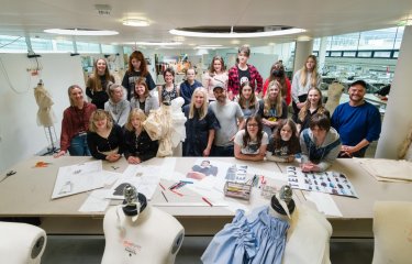 A group of teenagers showcase their artwork - sketches and mannequins with clothing are visible 