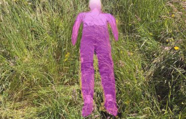 image: @josiecockram ‘after Ana Mendieta’. A field of grass with purple person lying in the grass