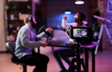View of SLR camera filming two people in conversation around a table