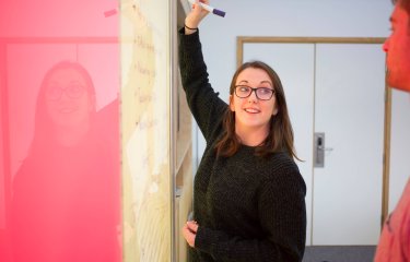 Student writing on a vibrant pink and yellow wall board, Falmouth University