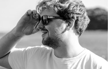 A man looks to his left, wearing sunglasses. The picture is in black and white