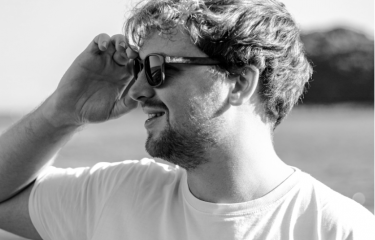 A man looks to his left, wearing sunglasses. The picture is in black and white