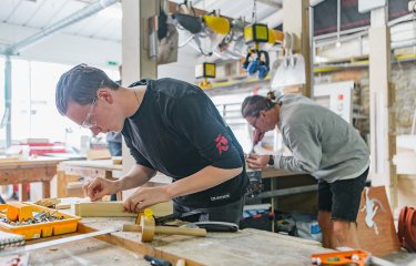 A couple of people working with wood at workshop benches