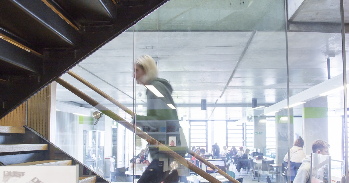 Female student walking up a staircase behind glass