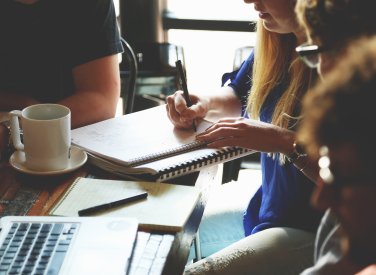 Business students sat around a desk, taking notes and drinking coffee.