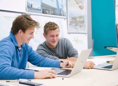 Two male students seated while looking at a laptop
