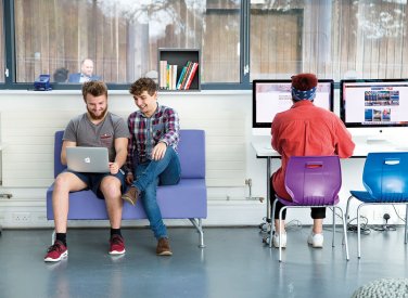 Three business management students working at a laptop and desktop