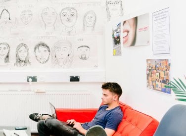 Male Creative Advertising student sitting on a red sofa at Falmouth University