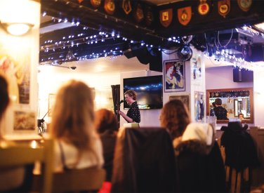 Student speaking into microphone at event in pub surrounded by blue fairy lights.