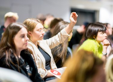 Female student raising hand in a crowd
